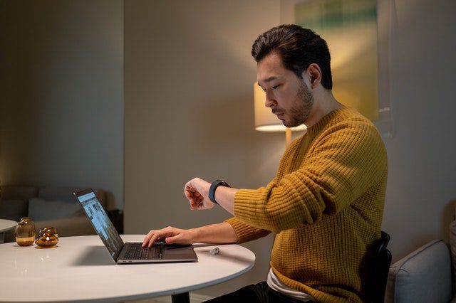 A person looking at a watch while working on a laptop