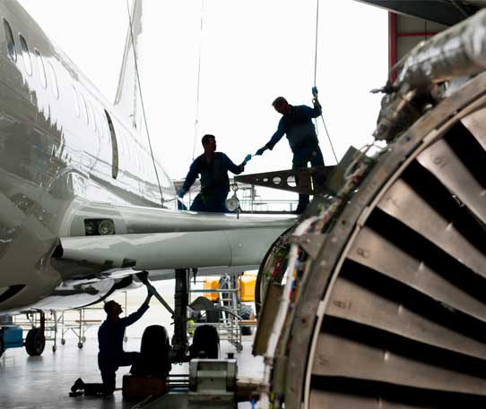 Aerospace technicians performing aircraft maintenance and engine inspection inside a hangar, representing precision aerospace logistics and maintenance operations.