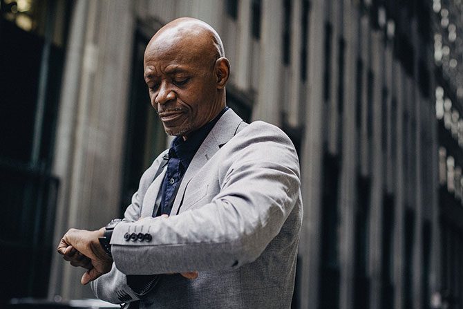 A man in a business suit looking at his watch while thinking about how to deal with shipping delays