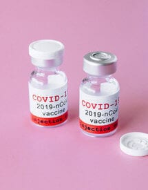 Vaccines for COVID-19 on a pink surface.