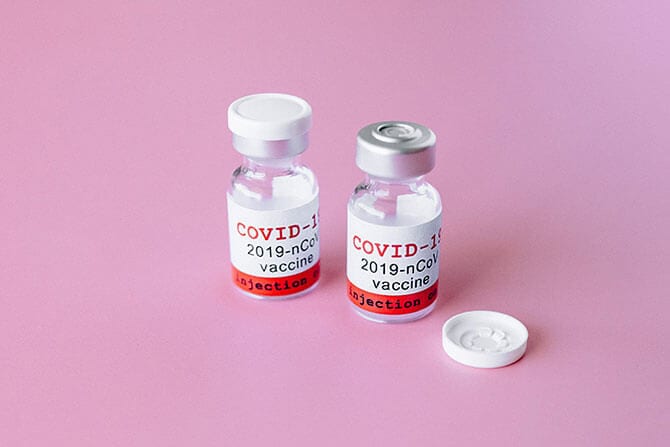 Vaccines for COVID-19 on a pink surface.