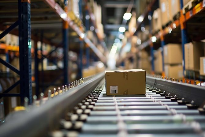 Cardboard box moving along a conveyor belt in a warehouse, symbolizing supply chain operations and transportation logistics, highlighting challenges in demand volatility and supplier disruptions.